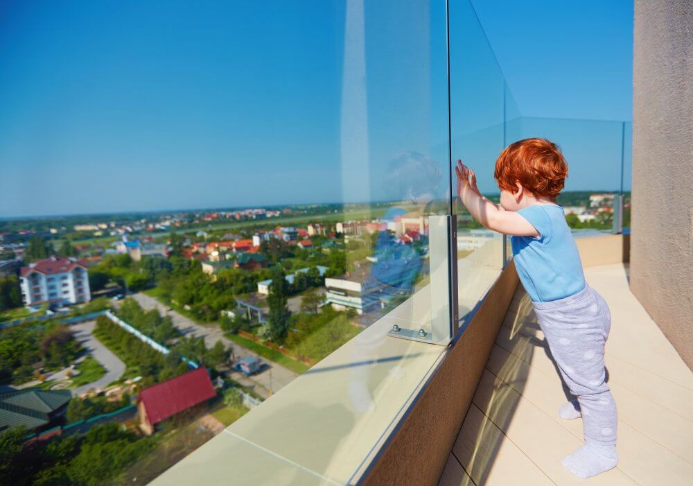 Malé ryšavé dieťa opreté o sklenené zábradlie pozerajúce sa na výhľad.